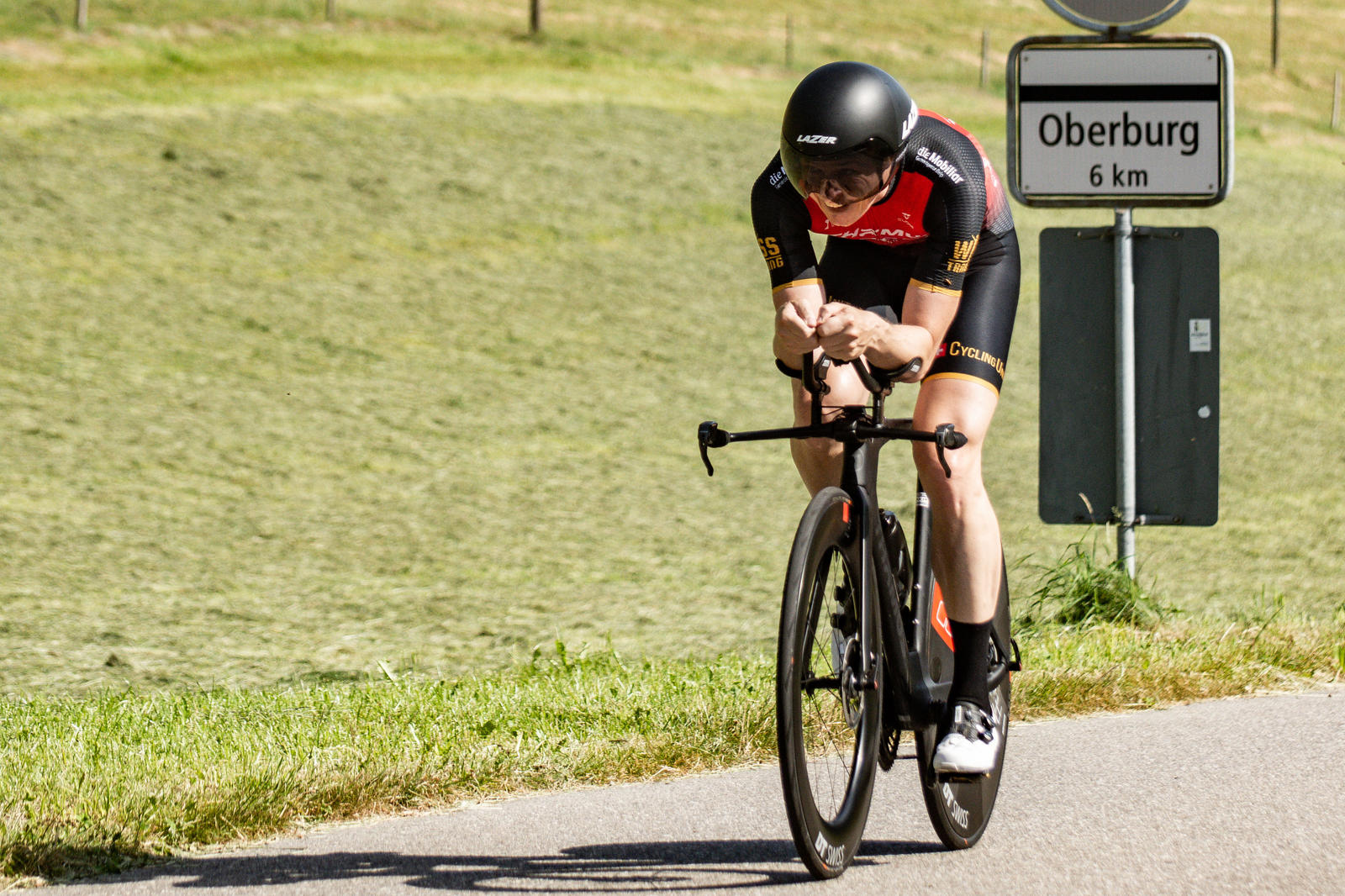 Zeitfahrer auf dem Zeitfahrvelo neben dem Wegweiser nach Oberburg